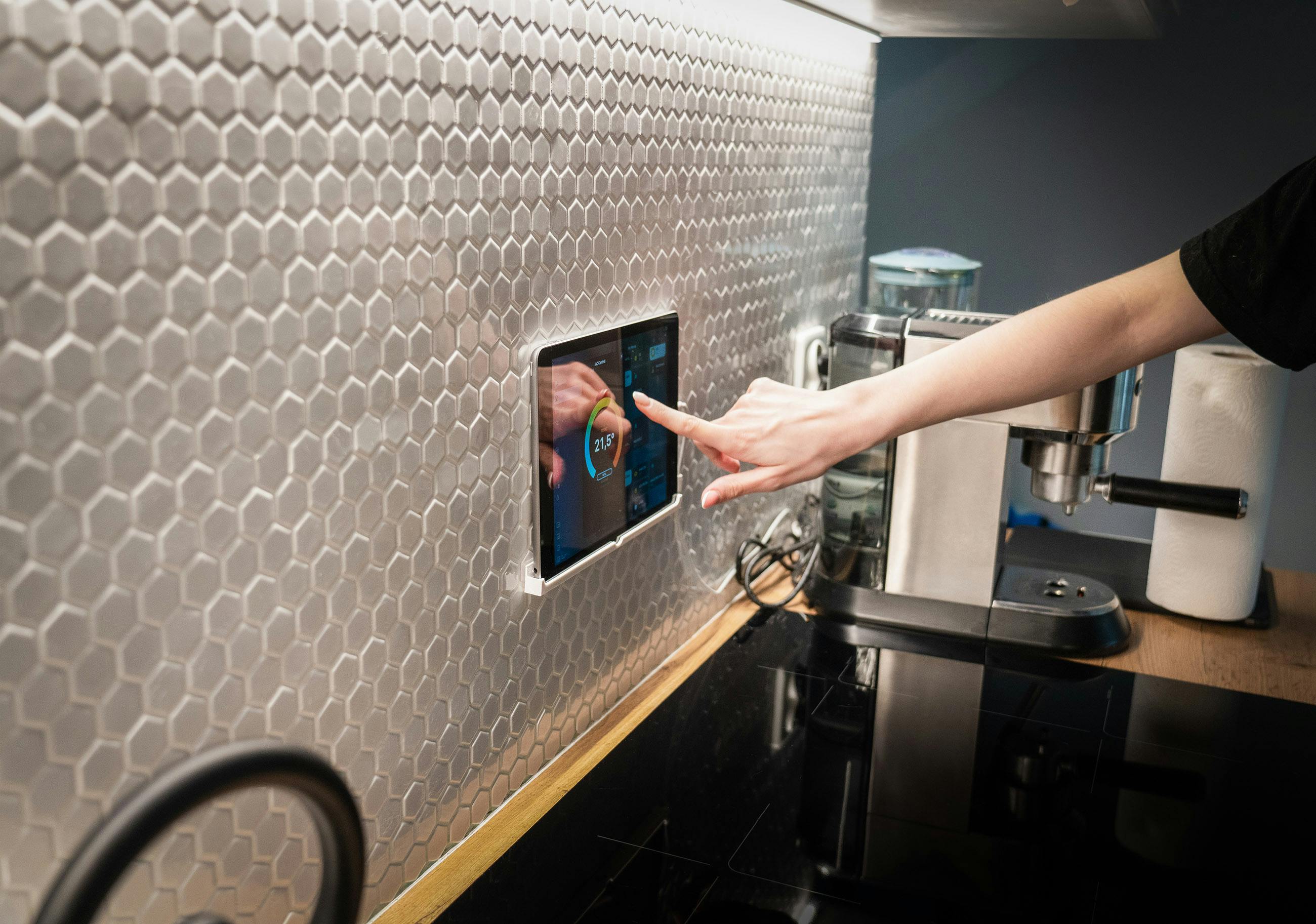 Person using an energy-efficient smart home control panel mounted on a modern kitchen backsplash.